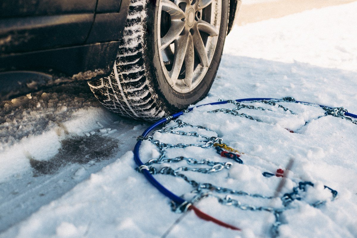 Οδηγός τοποθετεί αντιολισθητικές αλυσίδες σε ελαστικό αυτοκινήτου σε χιονισμένο δρόμο