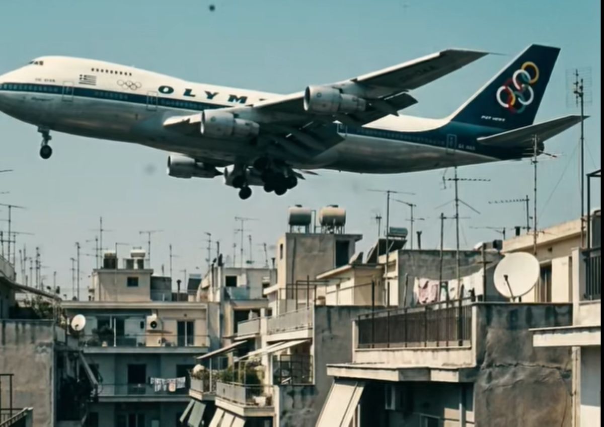 Αναπαράσταση του Boeing 747 της Ολυμπιακής να πετά σε χαμηλό ύψος πάνω από τις πολυκατοικίες στην Καλλιθέα