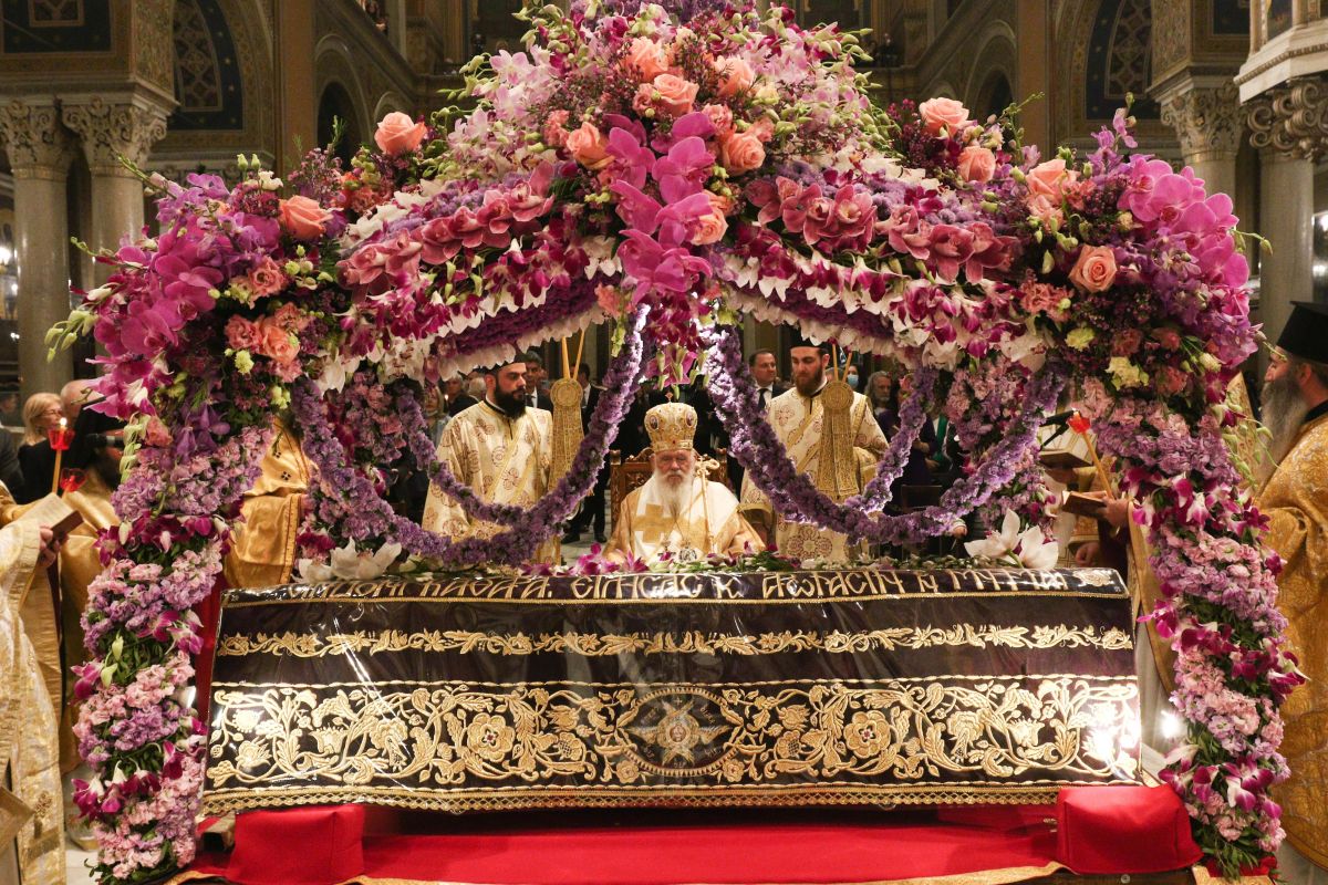 Ένας παραδοσιακός ξυλόγλυπτος Επιτάφιος στολισμένος με βιολέτες και τριαντάφυλλα μέσα σε ορθόδοξο ναό