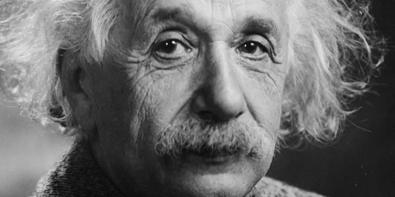 Ο Άλμπερτ Αϊνστάιν χαμογελαστός με φόντο έναν μαυροπίνακα, συμβολίζοντας τη δημιουργική ευφυΐα